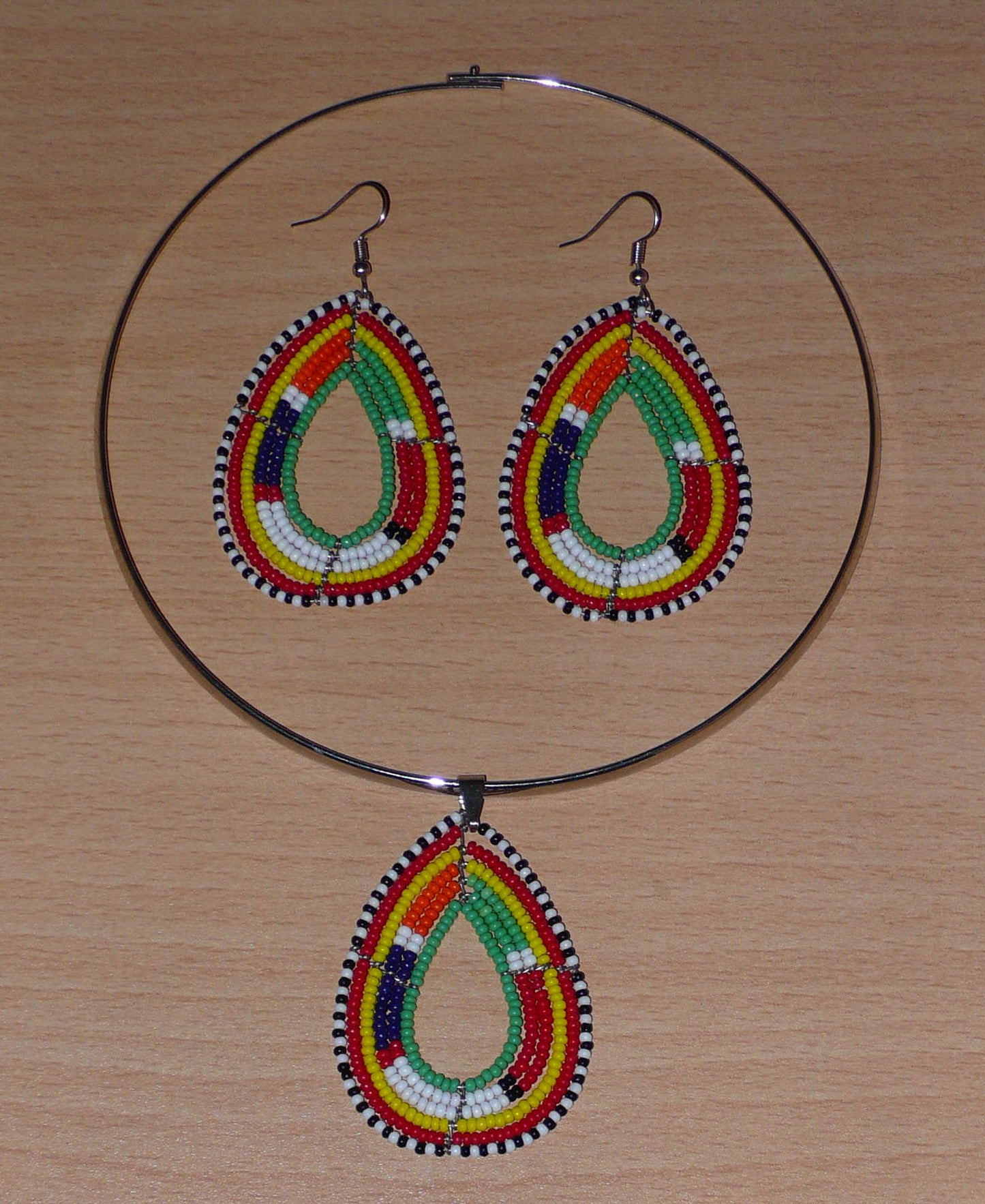 Parure de bijoux africains aux couleurs et motifs Massai composée d'un collier ras de cou en laiton agrémenté d'un pendentif en forme de goutte fait de perles de rocaille vertes et multicolores, et d'une paire de boucles d'oreilles assorties.