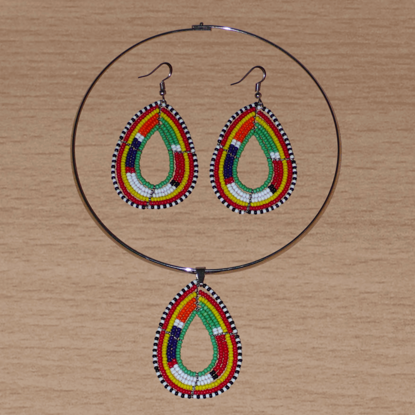 Parure de bijoux africains aux couleurs et motifs Massai composée d'un collier ras de cou en laiton agrémenté d'un pendentif en forme de goutte fait de perles de rocaille vertes et multicolores, et d'une paire de boucles d'oreilles assorties.