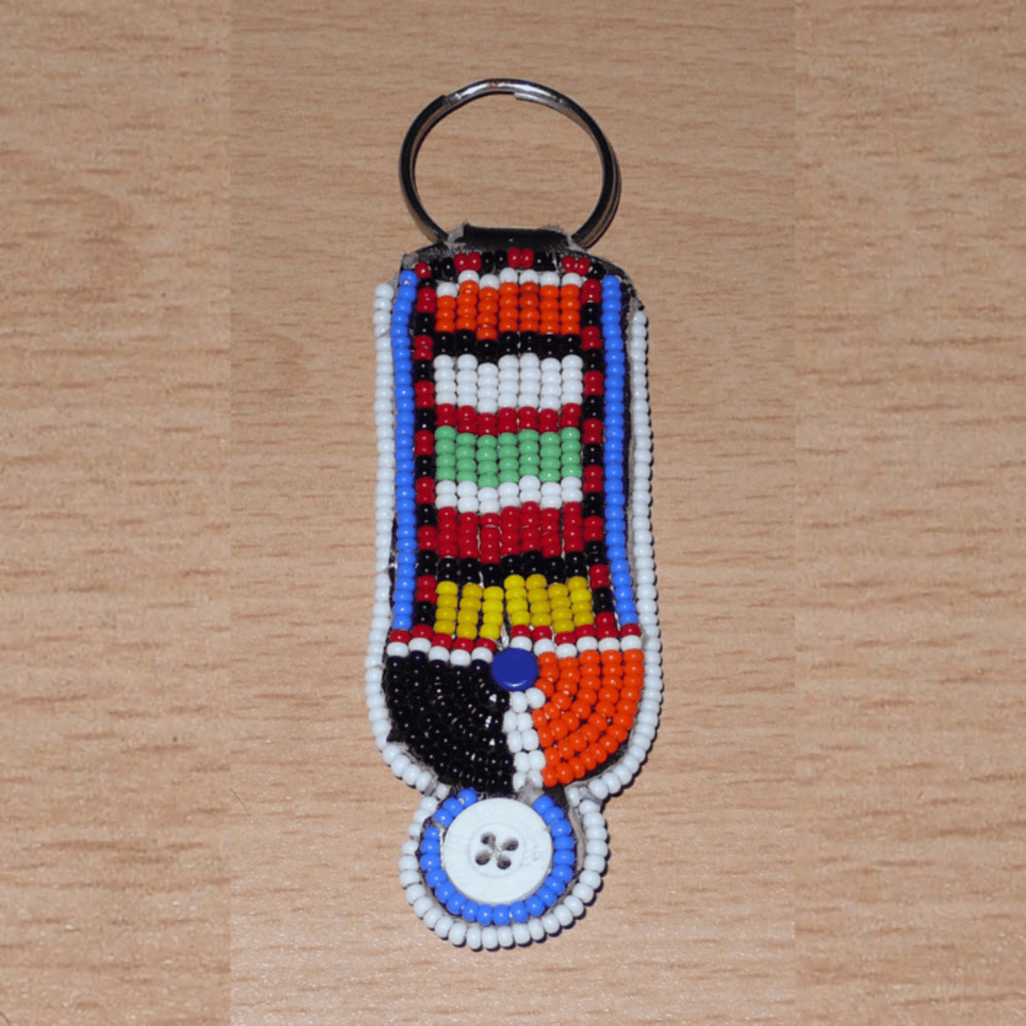 Porte-clés africain à motifs traditionnels Massai composé de perles de rocaille multicolores et de boutons brodés sur un morceau de cuir. Ce porte-clés, brodé sur les deux faces, mesure 10,5 cm de long et 3 cm de large.