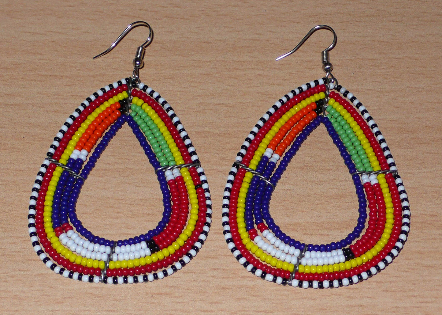 Longues boucles d'oreilles africaines traditionnelles Massai en perles de rocaille bleu foncé et multicolores glissées sur six rangées de fils de fer montés en forme de triangles. Elles mesurent 8,5 cm de long et 5 cm de large et se portent sur des oreilles percées.