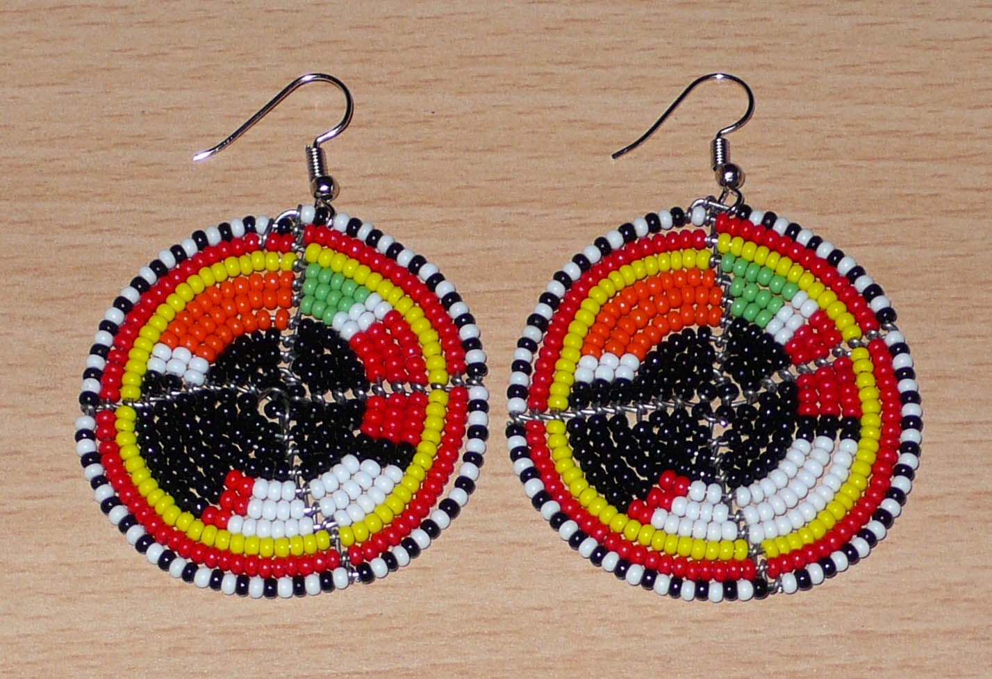 Boucles d'oreilles ethniques rondes composées de perles de rocaille noires et multicolores. De taille moyenne, ces boucles d'oreilles africaines de tradition Massai mesurent 6,5 cm de long et 4,5 cm de large ; elles se portent avec des crochets en acier inoxydable sur des oreilles percées.