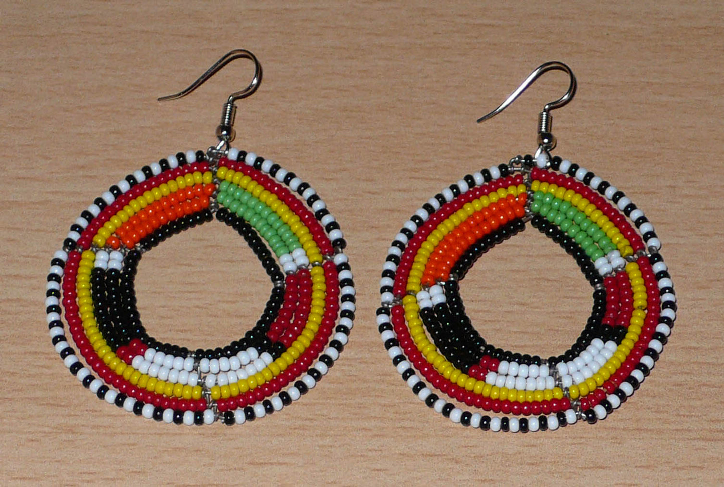 Boucles d'oreilles africaines à motifs ethniques Massai composées de perles de rocaille noires et multicolores fixées sur six rangées de fils de fer montés en cercles. De taille moyenne, elles mesurent 7 cm de long et 5 cm de large et se portent sur des oreilles percées.
