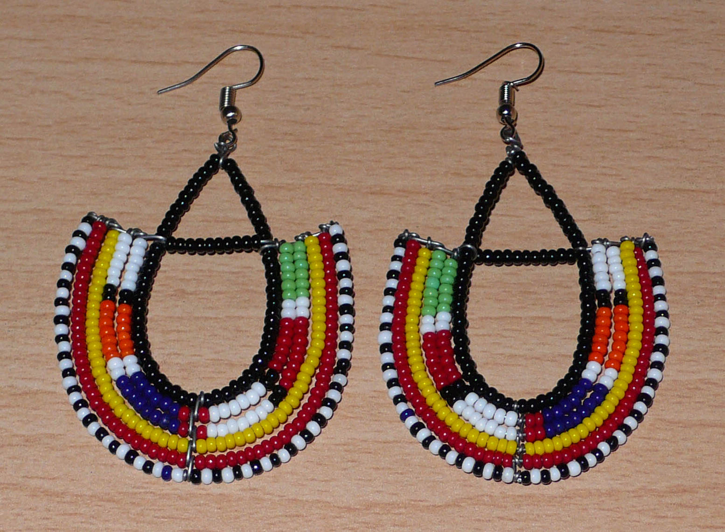 Boucles d'oreilles africaines traditionnelles fabriquées au Kenya par des femmes de la tribu Massai ; elles se composent de perles de rocaille noires et multicolores montées en forme d'ancres, et mesurent 7,5 cm de long et 4,5 cm de large. Elles se portent sur des oreilles percées avec des crochets en acier inoxydable.