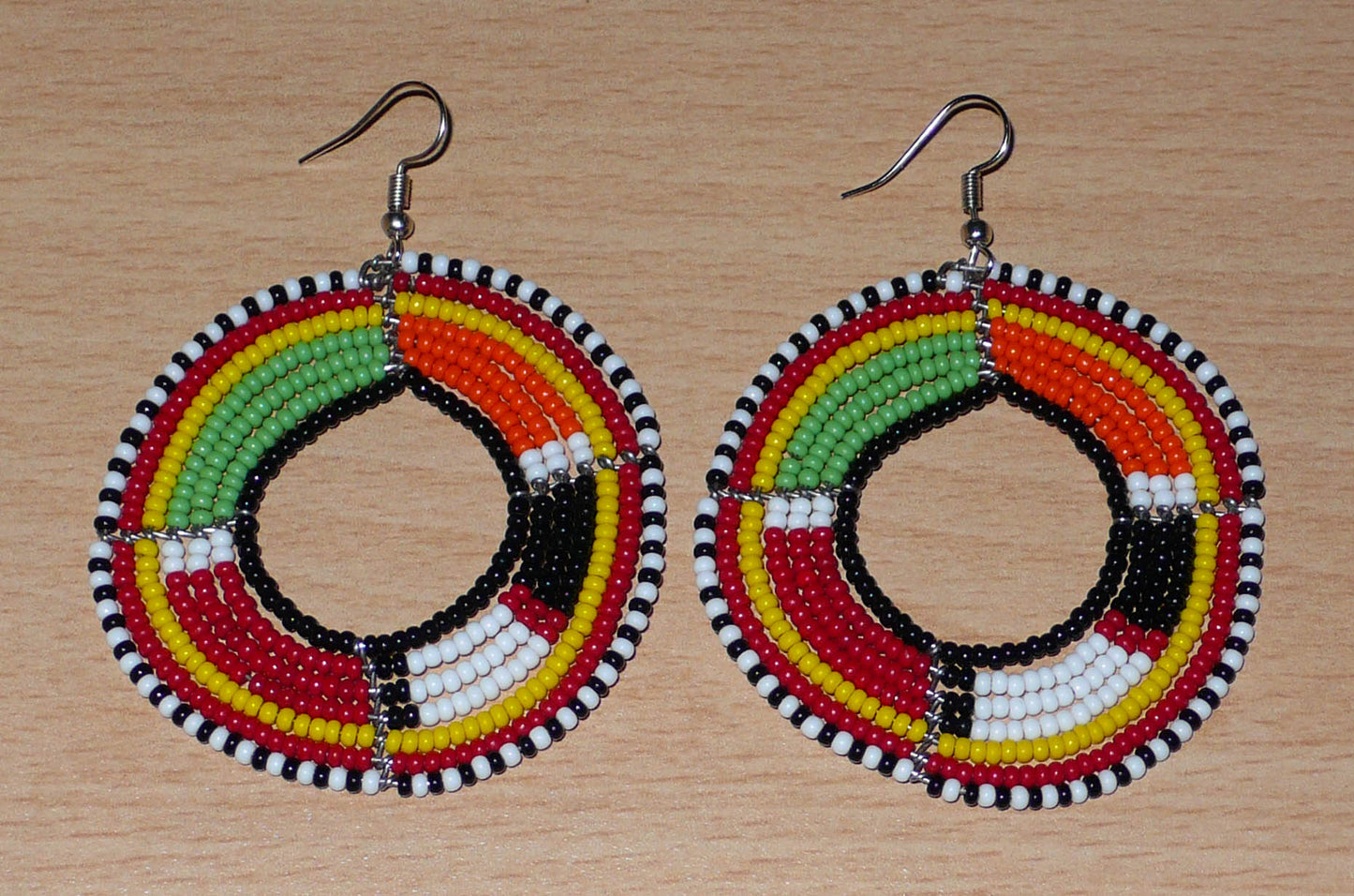 Boucles d'oreilles africaines à motifs ethniques Massai composées de perles de rocaille multicolores montées en forme de cercles. Elles mesurent 7,5 cm de long et 5,5 cm de large et se portent avec des crochets en acier inoxydable sur des oreilles percées.