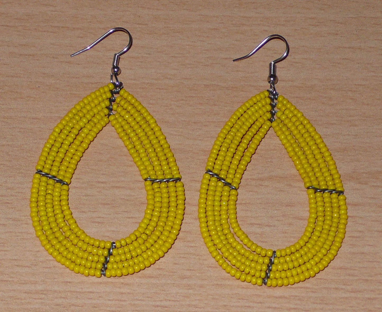 Boucles d'oreilles jaunes en forme de gouttes composées de perles de rocaille. Elles mesurent 8 cm de long et 4,5 cm de large, et se portent avec des crochets en acier inoxydable sur des oreilles percées.