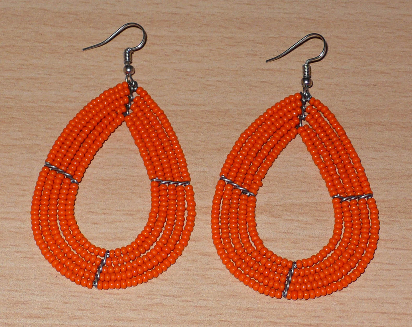 Boucles d'oreilles multi-rangs orange en forme de gouttes composées de perles de rocaille. Elles mesurent 8 cm de long et 4,5 cm de large, et se portent sur des oreilles percées.