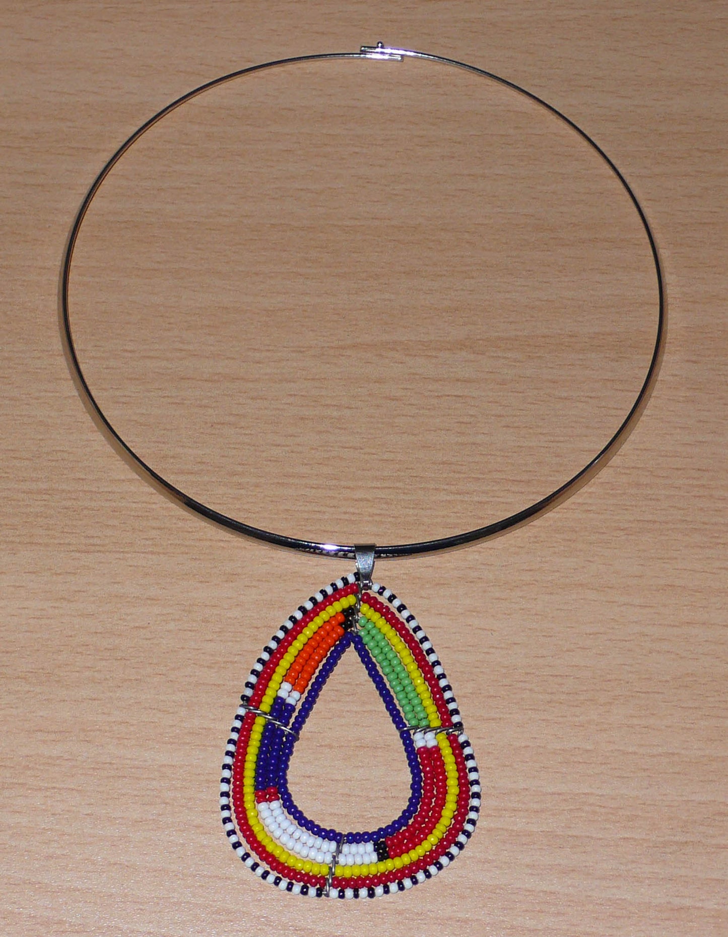 Collier africain composé d'un ras de cou en laiton agrémenté d'un pendentif Massai fait de perles de rocaille bleu foncé et multicolores.