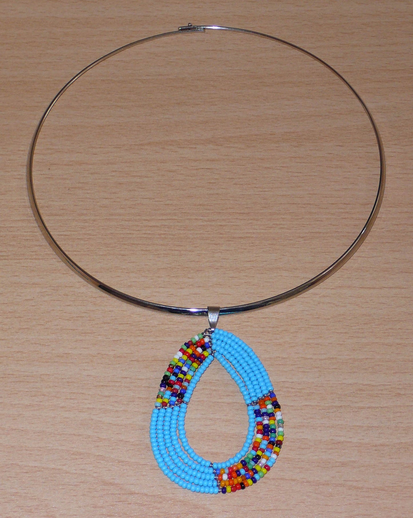 Collier ethnique bleu composé d'un ras de cou en laiton agrémenté d'un pendentif fait de perles de rocaille bleu ciel et multicolores enfilées sur cinq rangées de fils de fer montés en forme de goutte.