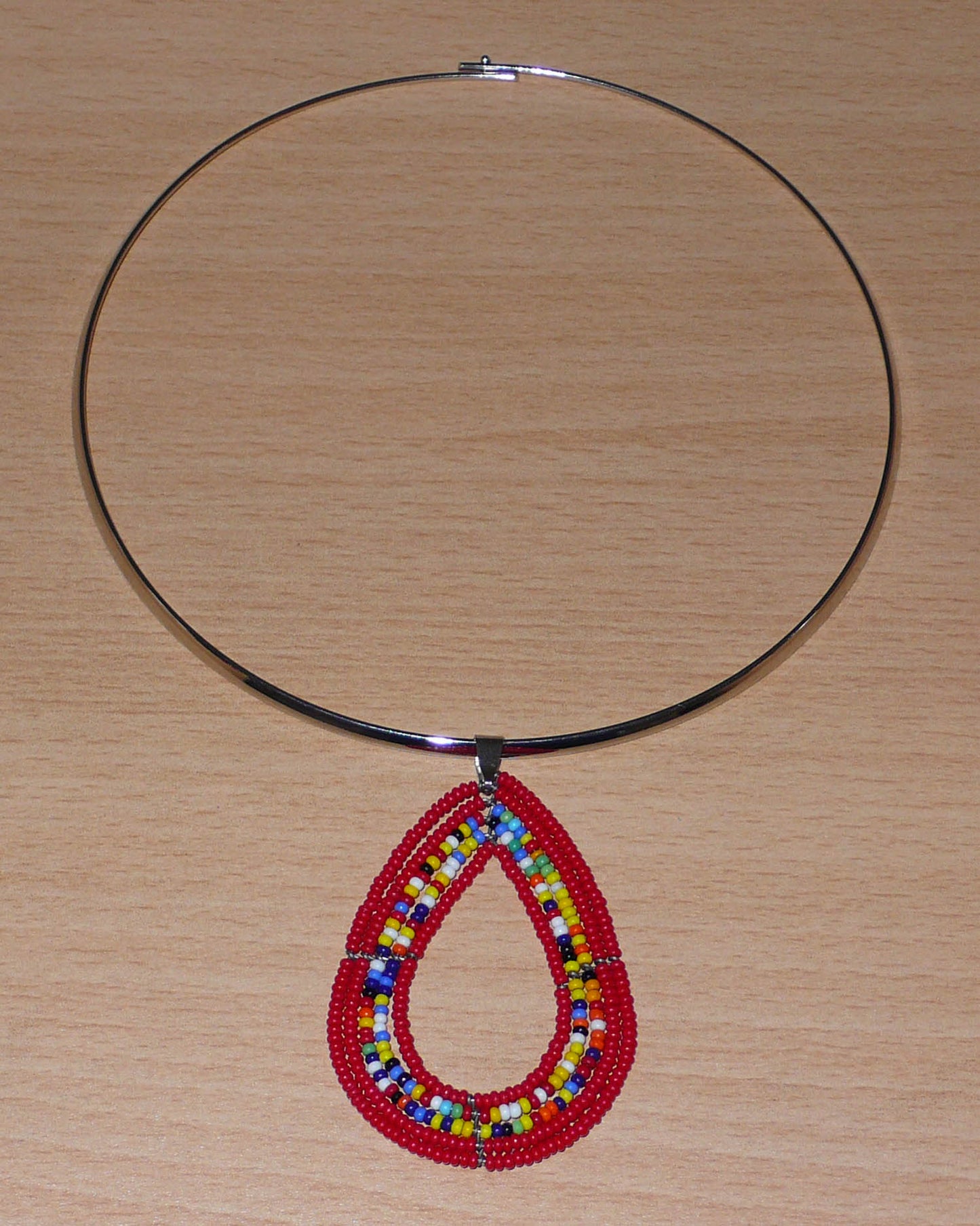 Collier ethnique de style afro bohème composé d'un ras de cou en laiton orné d'un pendentif en forme de goutte fait de perles de rocaille rouges et multicolores. Il mesure 20 cm de long, la circonférence du ras de cou en laiton est de 42,5 cm et son diamètre de 13,5 cm ; le pendentif perlé mesure 7 cm de long et 4,5 cm de large.