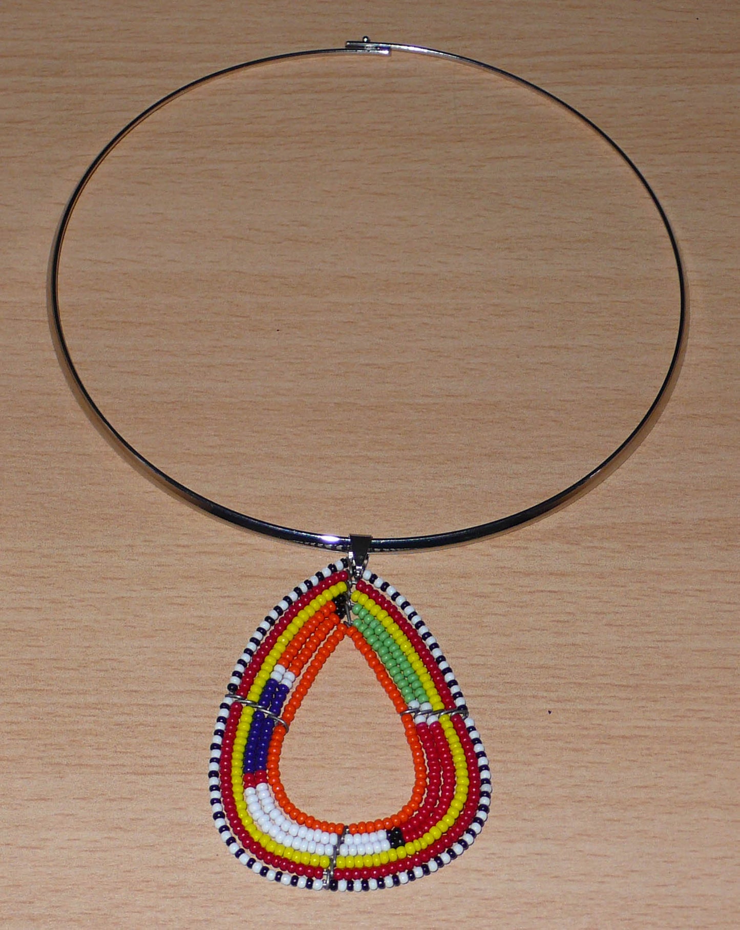 Collier africain composé d'un ras de cou en laiton orné d'un pendentif Massai fait de perles de rocaille orange et multicolores montées en forme de triangle aux bords arrondis.