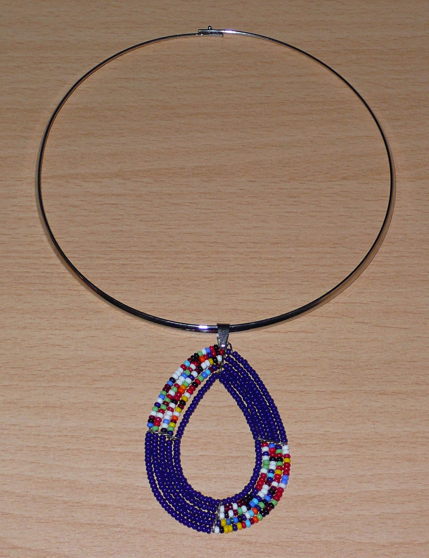 Collier ethnique chic bleu composé d'un ras de cou en laiton agrémenté d'un long pendentif Massai fait de perles de rocaille bleu foncé et multicolores montées en forme de goutte.