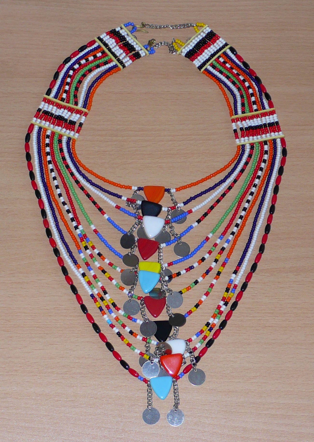 Collier africain traditionnel Massai composé de plusieurs rangées de perles multicolores ; des perles triangulaires et des pastilles en métal décorent le collier en son centre.