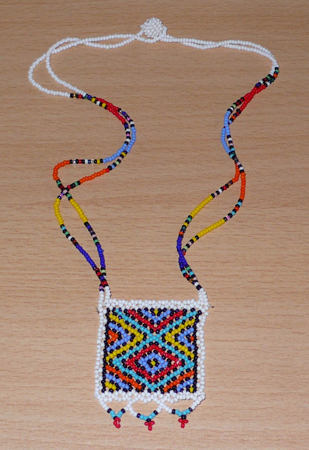 Collier africain zoulou en perles de rocaille blanches et multicolores agrémenté d'un pendentif carré à motifs ethniques traditionnels.