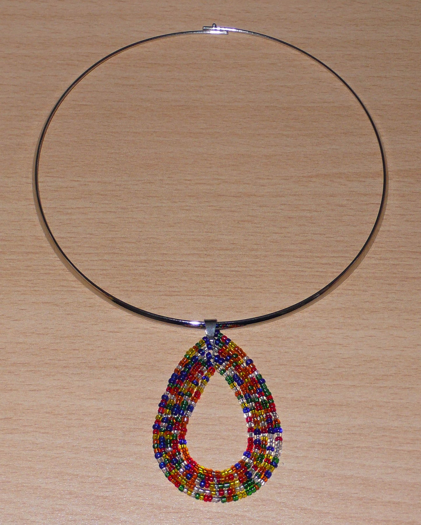Collier ethnique contemporain composé d'un ras de cou en laiton orné d'un pendentif fait d'un mélange de perles de rocaille multicolores translucides montées en forme de goutte.
