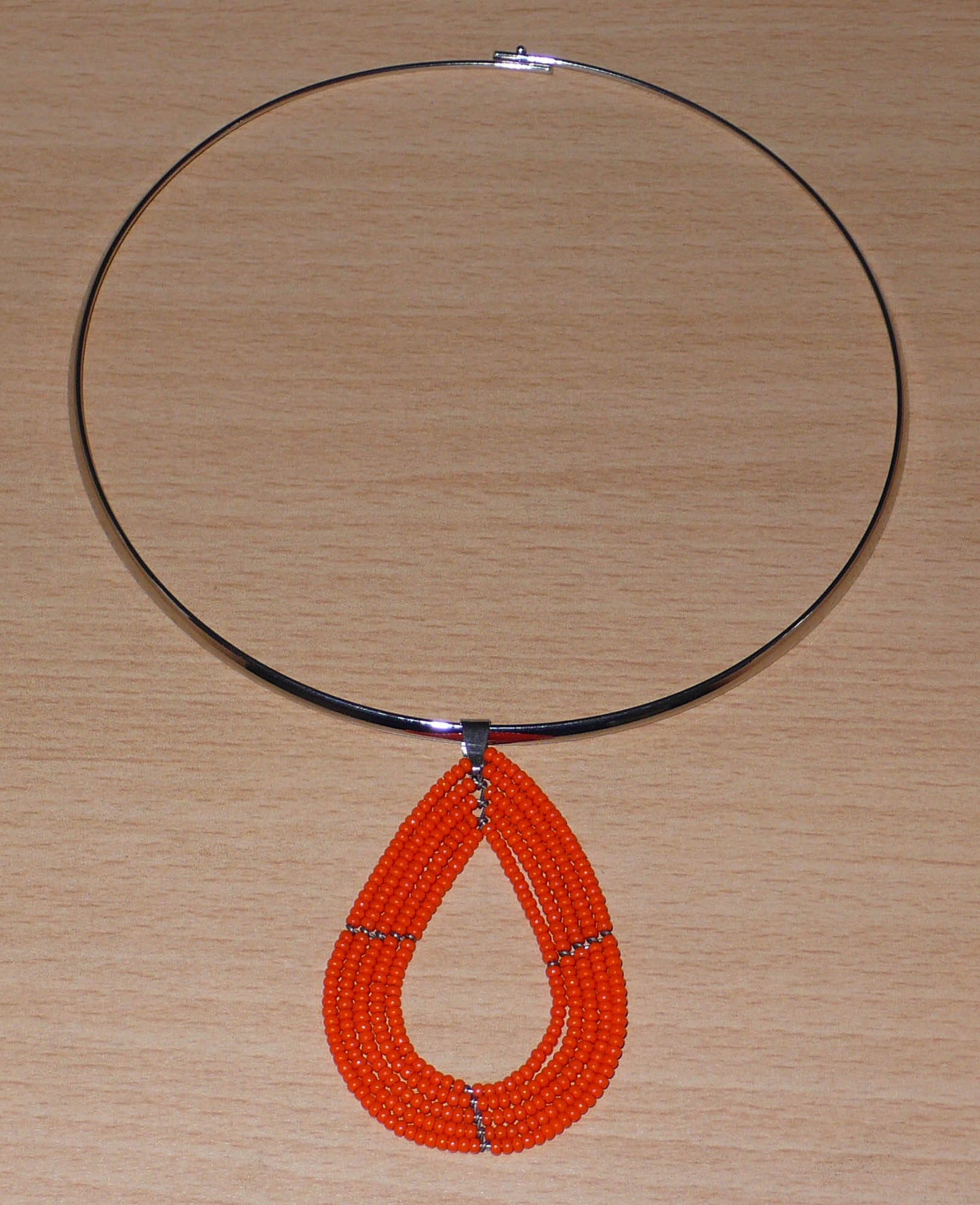 Collier ras de cou en laiton orné d'un pendentif en forme de goutte fait de perles de rocaille orange.