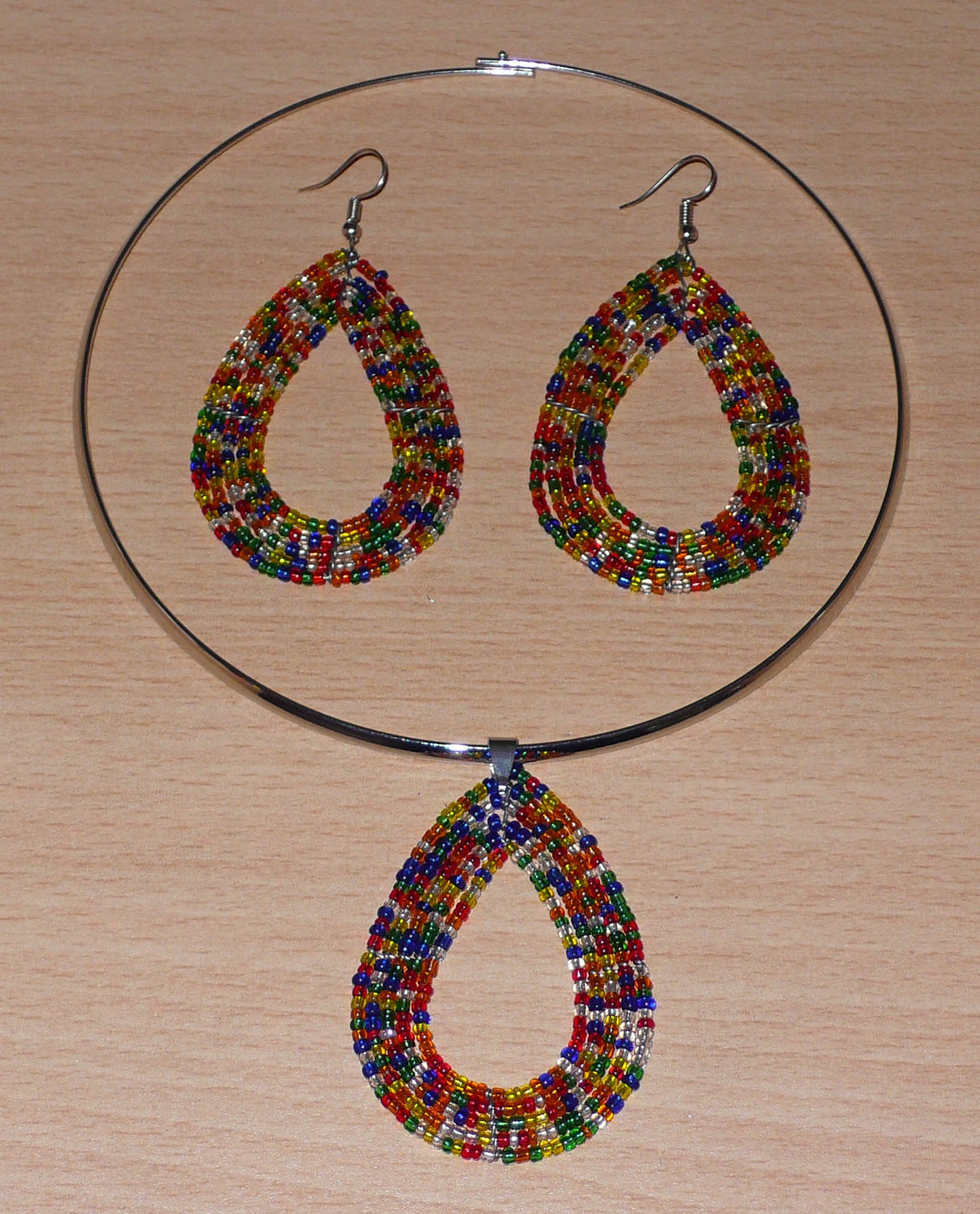 Parure contemporaine de bijoux ethniques composée d'un collier ras de cou en laiton agrémenté d'un pendentif en forme de goutte fait d'un mélange de perles de rocaille translucides multicolores, ainsi que d'une paire de boucles d'oreilles assorties au collier.