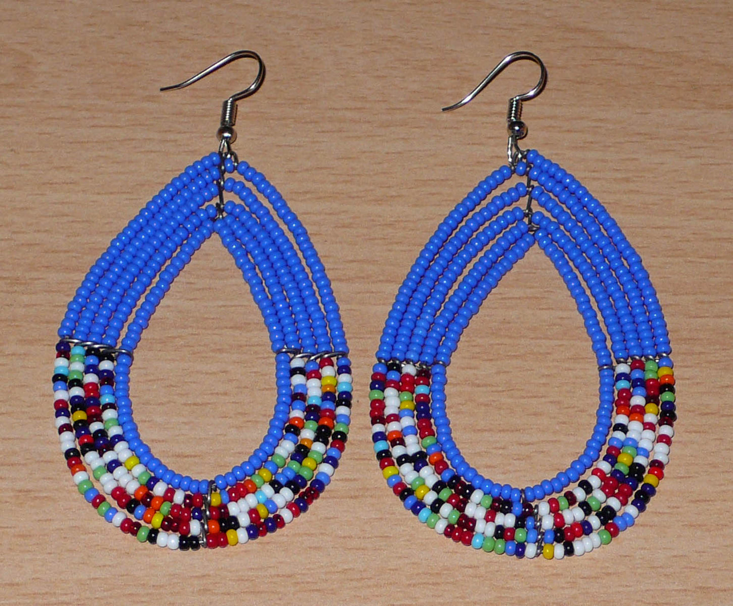 Longues boucles d'oreilles ethniques bleues et multicolores faites de perles de rocaille glissées sur cinq rangées de fils de fer montés en forme de gouttes. Elles mesurent 9 cm de long et 4,5 cm de large, et se portent avec des crochets en acier inoxydable sur des oreilles percées.