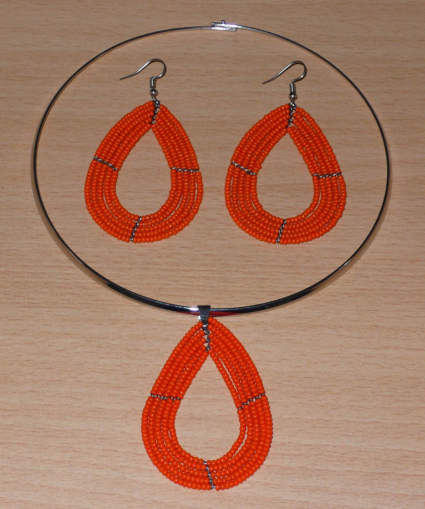 Parure de bijoux orange composée d'un collier ras de cou en laiton orné d'un pendentif en forme de goutte fait de perles de rocaille, et d'une paire de boucles d'oreilles assorties.