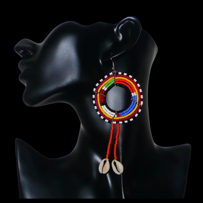 Longues boucles d'oreilles africaines Massai rondes à franges perlées, composées de perles de rocaille orange et multicolores et de coquillages cauris. Elles mesurent 12 cm de long et 5 cm de large, et se portent sur des oreilles percées.