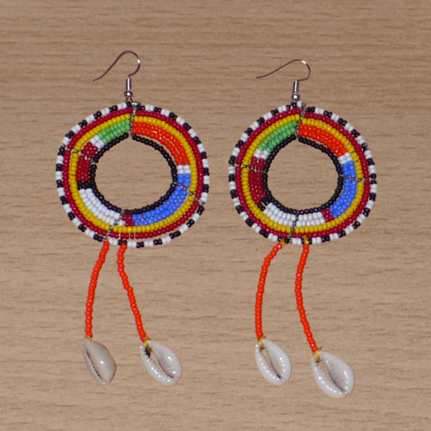 Longues boucles d'oreilles africaines Massai rondes à franges perlées, composées de perles de rocaille orange et multicolores et de coquillages cauris. Elles mesurent 12 cm de long et 5 cm de large, et se portent sur des oreilles percées.