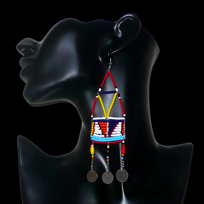 Longues boucles d'oreilles africaines à motifs géométriques Massai composées de perles de rocaille et de plastique rouges et multicolores, et de chaînettes décorées de perles et de disques métalliques. Elles mesurent 13 cm de long et 4 cm de large et se portent sur des oreilles percées.