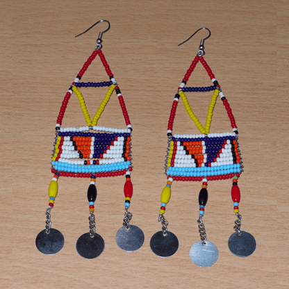 Longues boucles d'oreilles africaines à motifs géométriques Massai composées de perles de rocaille et de plastique rouges et multicolores, et de chaînettes décorées de perles et de disques métalliques. Elles mesurent 13 cm de long et 4 cm de large et se portent sur des oreilles percées.