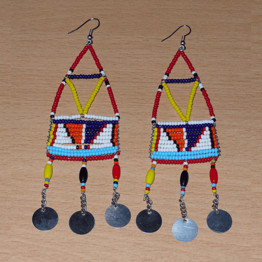 Longues boucles d'oreilles africaines à motifs géométriques Massai composées de perles de rocaille et de plastique rouges et multicolores, et de chaînettes décorées de perles et de disques métalliques. Elles mesurent 13 cm de long et 4 cm de large et se portent sur des oreilles percées.
