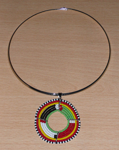 Bijou africain composé d'un collier ras de cou en laiton orné d'un médaillon Massai fait de perles de rocaille rouges, vertes, jaunes, blanches et noires enfilées sur sept rangées de fils de fer montés en cercles. Il mesure 19 cm de long, la circonférence du ras de cou en laiton est de 42,5 cm et 13,5 cm de diamètre ; le pendentif mesure 5,5 cm de long et de large.