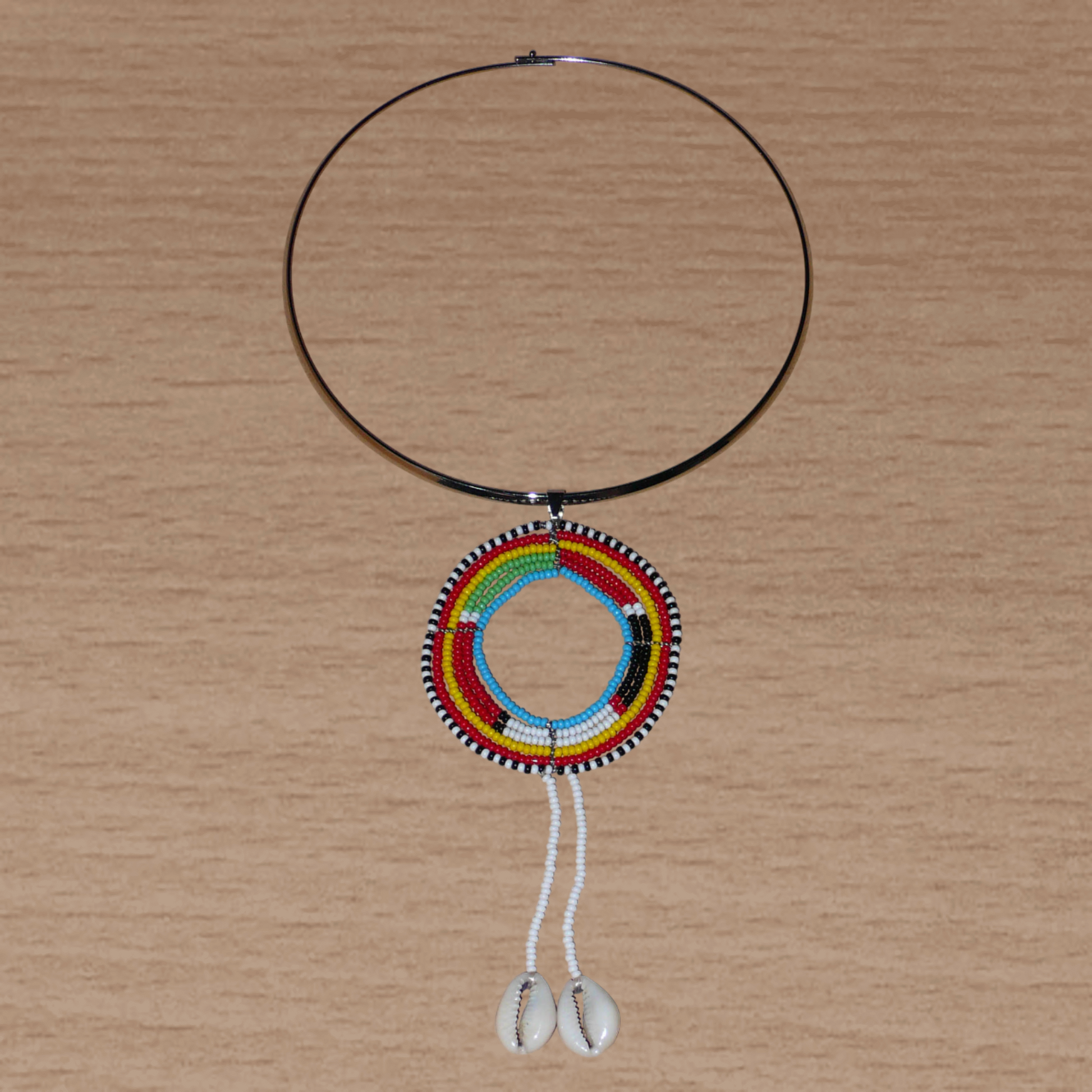 Collier africain aux accents exotiques composé d'un ras de cou en laiton orné d'un long pendentif ethnique Massai fait de perles de rocaille et de coquillages cauris.