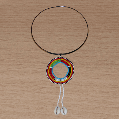 Collier africain aux accents exotiques composé d'un ras de cou en laiton orné d'un long pendentif ethnique Massai fait de perles de rocaille et de coquillages cauris.