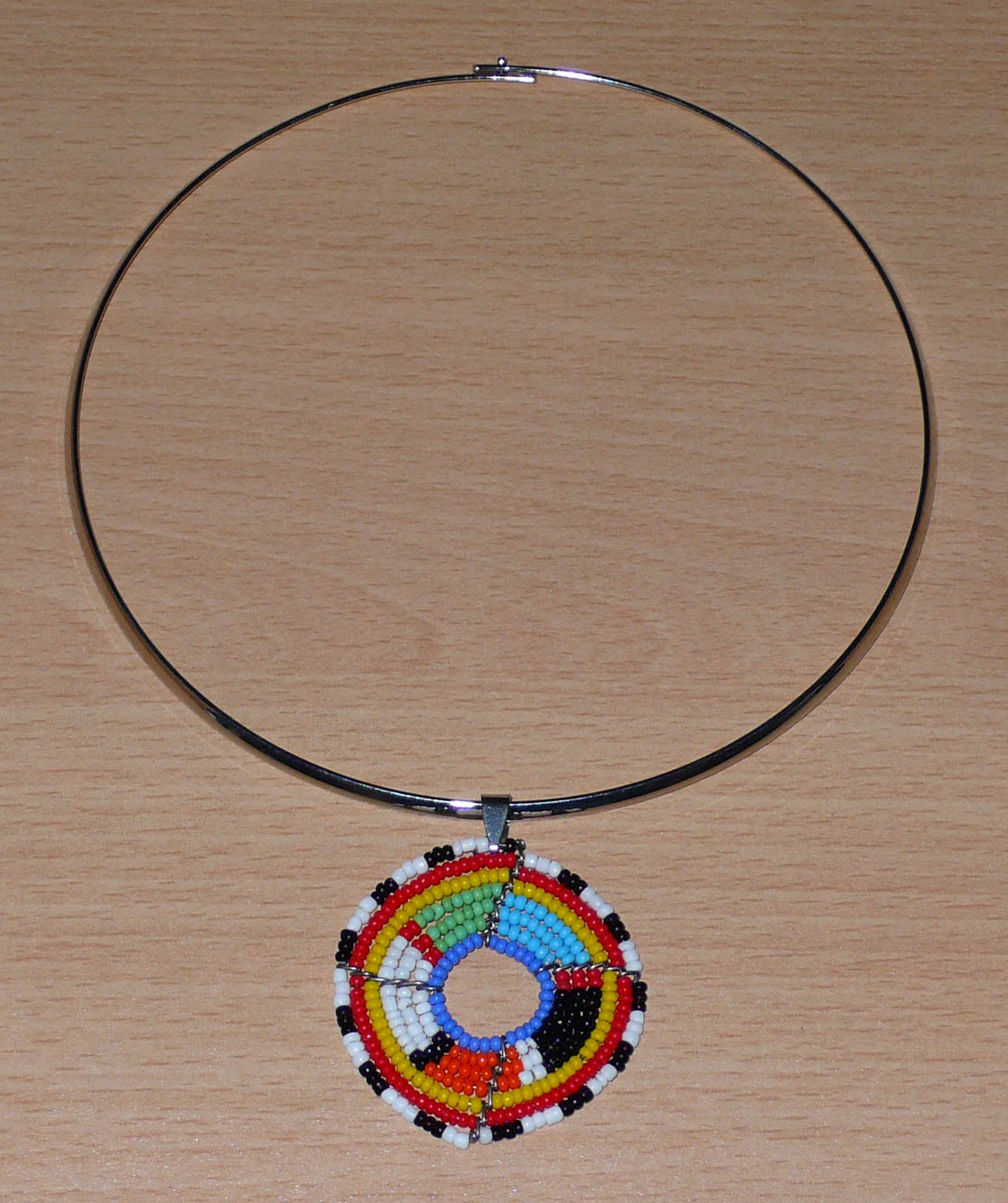 Bijou africain contemporain composé d'un ras de cou en laiton orné d'un médaillon à motifs ethniques Massai fait d'un tissage de perles multicolores.