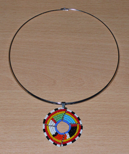 Bijou africain contemporain composé d'un ras de cou en laiton orné d'un médaillon à motifs ethniques Massai fait d'un tissage de perles multicolores.