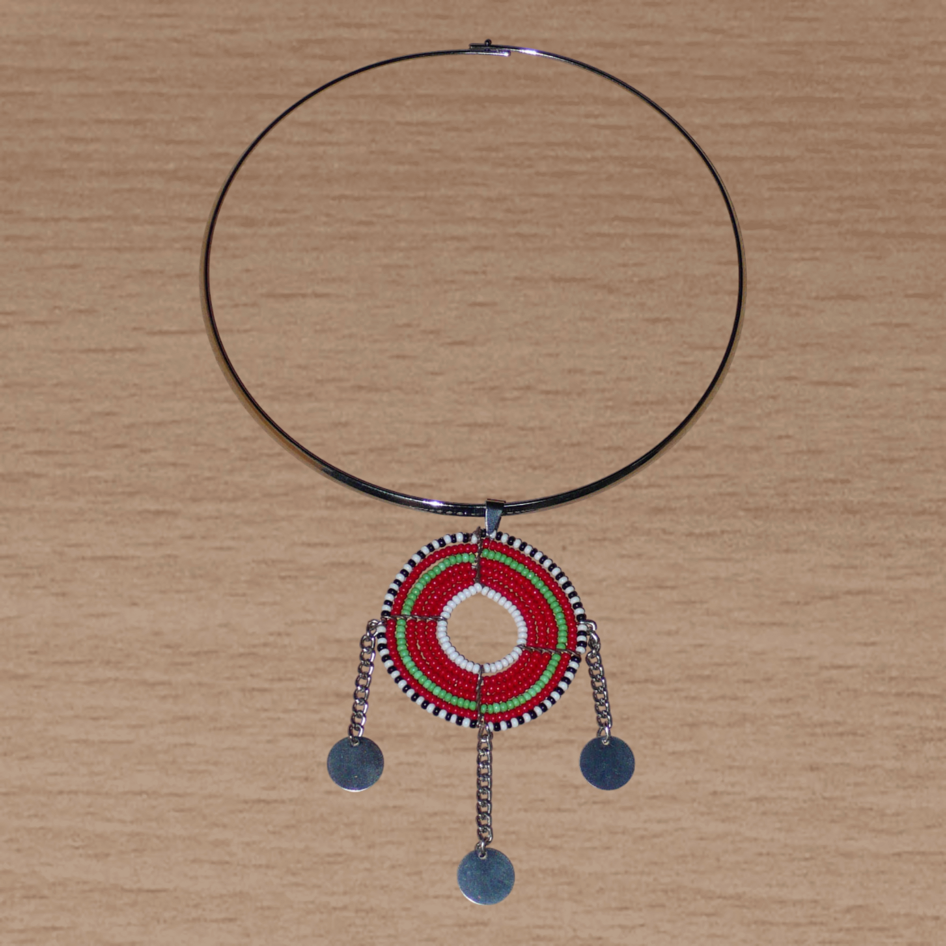 Bijou africain ethnique chic se composant d'un ras de cou en laiton agrémenté d'un beau pendentif Massai de forme ronde fait de perles de rocaille principalement rouges et vertes, et prolongé de trois chaînettes décorées de disques métalliques.