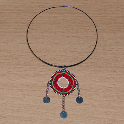 Bijou africain ethnique chic se composant d'un ras de cou en laiton agrémenté d'un beau pendentif Massai de forme ronde fait de perles de rocaille principalement rouges et vertes, et prolongé de trois chaînettes décorées de disques métalliques.