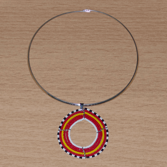 Bijou ethnique chic aux accents rétro composé d'un collier ras de cou en laiton agrémenté d'un large pendentif rond fait de perles de rocaille rouges, jaunes, blanches et noires.