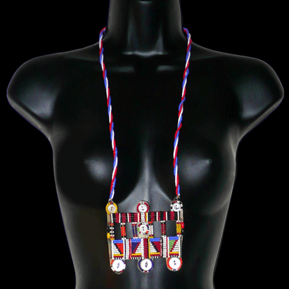 Collier africain traditionnel Massai de style sautoir composé d'une triple chaîne torsadée en perles de rocaille bleues, blanches et rouges ornée d'un large pendentif à motifs ethniques multicolores brodés de perles de rocaille et de boutons.