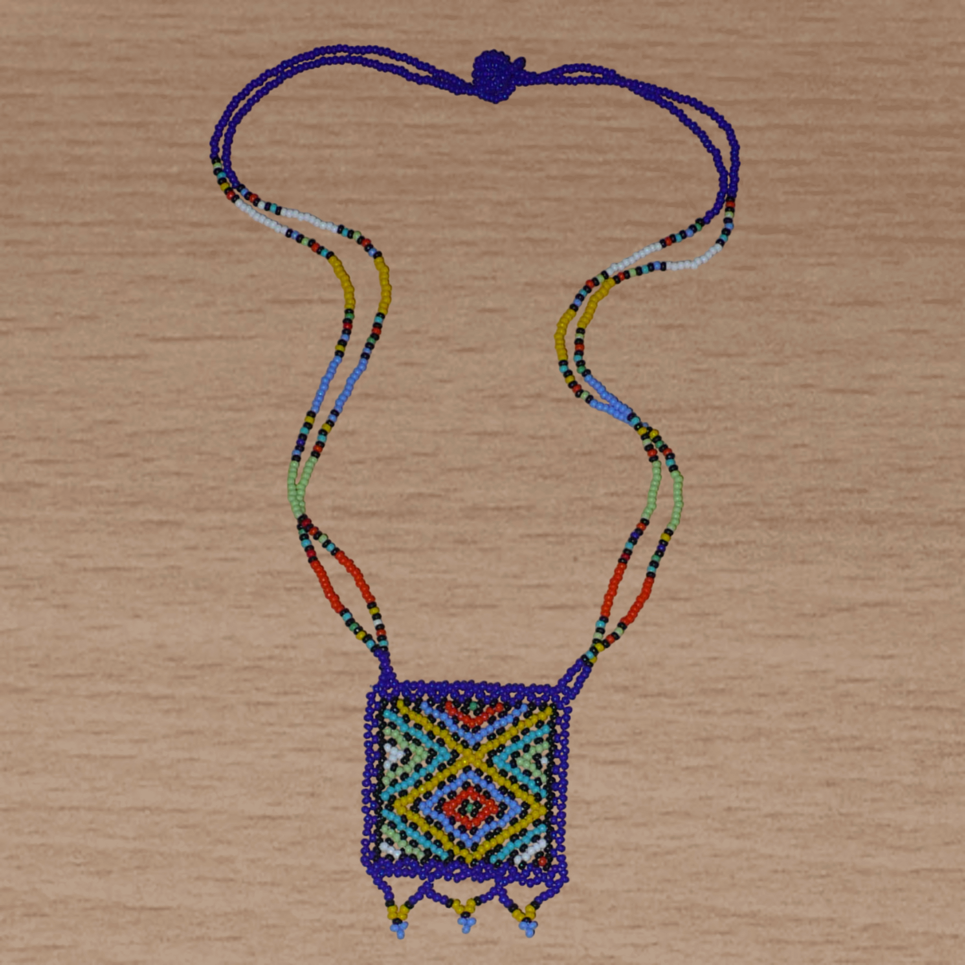 Collier africain avec pendentif à motifs ethniques ; de tradition sud-africaine, il est composé d'un tissage de perles de rocaille bleues et multicolores.