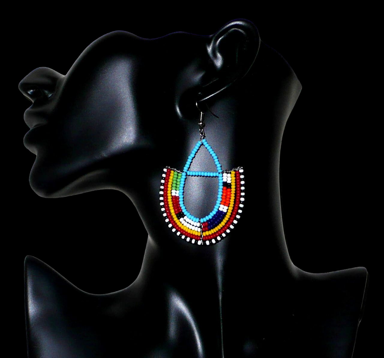Boucles d'oreilles africaines à motifs ethniques Massai fabriquées au Kenya. Elles se composent de perles de rocaille bleu ciel et multicolores montées en forme d'ancres. Ces boucles d'oreilles afro chic mesurent 7,5 cm de long et 4,5 cm de large. Elles se portent avec des crochets en acier inoxydable sur des oreilles percées.