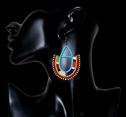 Boucles d'oreilles africaines à motifs ethniques Massai fabriquées au Kenya. Elles se composent de perles de rocaille bleu ciel et multicolores montées en forme d'ancres. Ces boucles d'oreilles afro chic mesurent 7,5 cm de long et 4,5 cm de large. Elles se portent avec des crochets en acier inoxydable sur des oreilles percées.