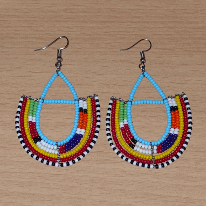 Boucles d'oreilles africaines à motifs ethniques Massai fabriquées au Kenya. Elles se composent de perles de rocaille bleu ciel et multicolores montées en forme d'ancres. Ces boucles d'oreilles afro chic mesurent 7,5 cm de long et 4,5 cm de large. Elles se portent avec des crochets en acier inoxydable sur des oreilles percées.