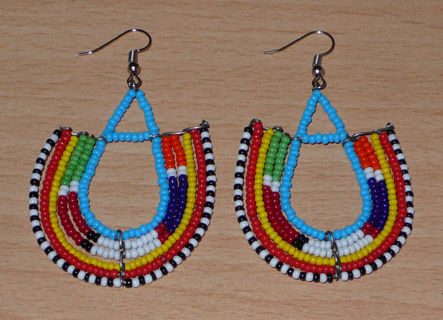 Boucles d'oreilles africaines traditionnelles à motifs ethniques Massai composées de perles de rocaille bleues et multicolores enfilées sur des fils de fer montés en forme d'ancres.

Ces boucles d'oreilles colorées au style exotique tribal chic mesurent 7.5 cm de long et 4.5 cm de large, elles se portent avec des crochets en acier inoxydable sur des oreilles percées.