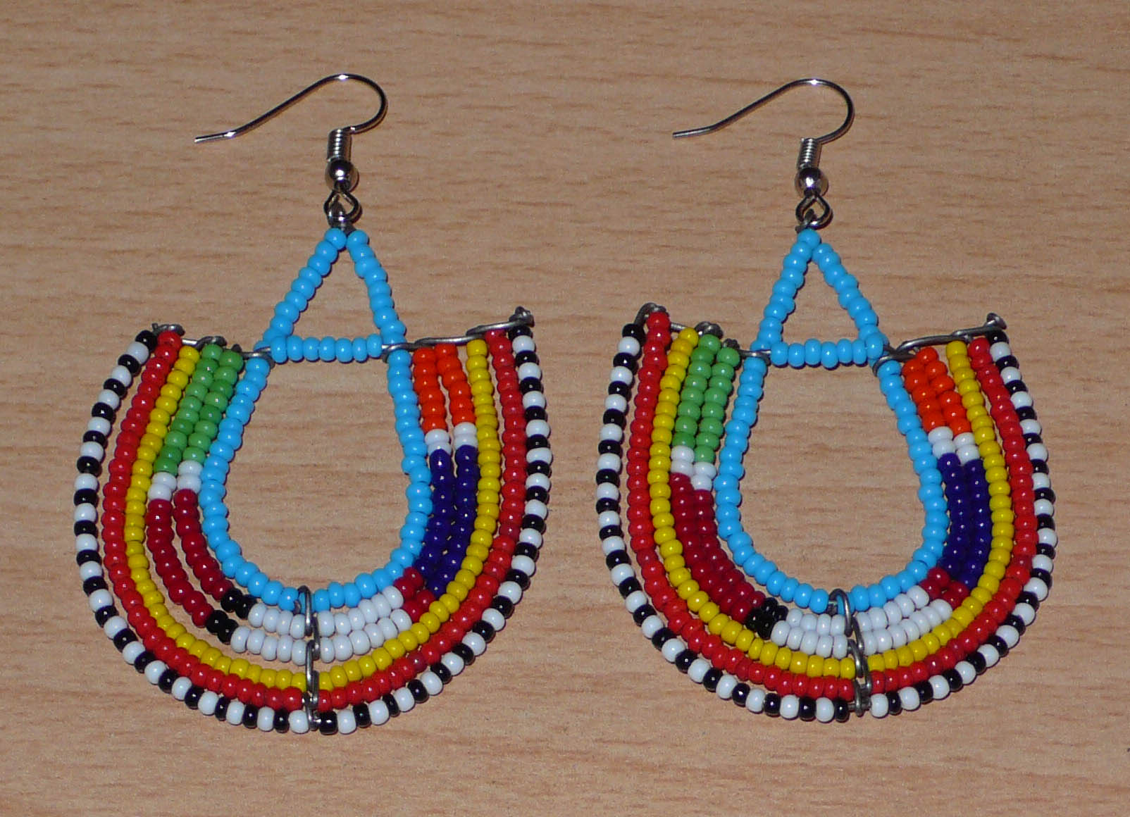 Boucles d'oreilles africaines traditionnelles à motifs ethniques Massai composées de perles de rocaille bleues et multicolores enfilées sur des fils de fer montés en forme d'ancres.

Ces boucles d'oreilles colorées au style exotique tribal chic mesurent 7.5 cm de long et 4.5 cm de large, elles se portent avec des crochets en acier inoxydable sur des oreilles percées.