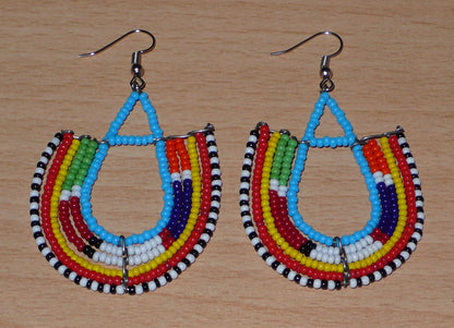 Boucles d'oreilles africaines traditionnelles à motifs ethniques Massai composées de perles de rocaille bleues et multicolores enfilées sur des fils de fer montés en forme d'ancres.

Ces boucles d'oreilles colorées au style exotique tribal chic mesurent 7.5 cm de long et 4.5 cm de large, elles se portent avec des crochets en acier inoxydable sur des oreilles percées.