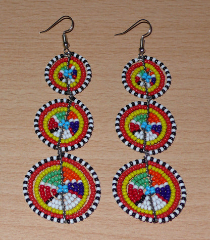 Ajoutez une touche colorée à votre look, évocatrice du style afro chic des années 70, avec ces boucles d'oreilles africaines traditionnelles de confection artisanale Massai. Elles se composent de perles de rocaille multicolores glissées sur des fils de fer montés en forme de trois cercles superposés. Ces boucles d'oreilles mesurent 10.5 cm de long et 3 cm de large ; elles se portent avec des crochets en acier inoxydable sur des oreilles percées.