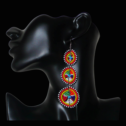 Ajoutez une touche colorée à votre look, évocatrice du style afro chic des années 70, avec ces boucles d'oreilles africaines traditionnelles de confection artisanale Massai. Elles se composent de perles de rocaille multicolores glissées sur des fils de fer montés en forme de trois cercles superposés. Ces boucles d'oreilles mesurent 10.5 cm de long et 3 cm de large ; elles se portent avec des crochets en acier inoxydable sur des oreilles percées.
