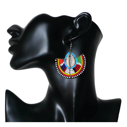 Affirmez votre style et apportez une touche exotique à votre look avec cette paire de boucles d'oreilles africaines Massai issues de l'artisanat traditionnel kenyan. Ces boucles d'oreilles aux accents ethniques chic se composent de perles de rocaille bleues et multicolores et de coquillages cauris. De taille moyenne, elles mesurent 6 cm de long et 4.5 cm de large, et se portent avec des crochets en acier inoxydable sur des oreilles percées.