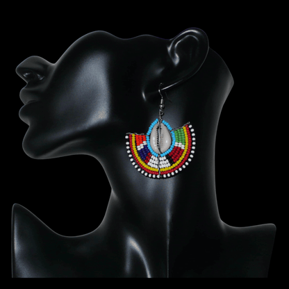 Affirmez votre style et apportez une touche exotique à votre look avec cette paire de boucles d'oreilles africaines Massai issues de l'artisanat traditionnel kenyan. Ces boucles d'oreilles aux accents ethniques chic se composent de perles de rocaille bleues et multicolores et de coquillages cauris. De taille moyenne, elles mesurent 6 cm de long et 4.5 cm de large, et se portent avec des crochets en acier inoxydable sur des oreilles percées.