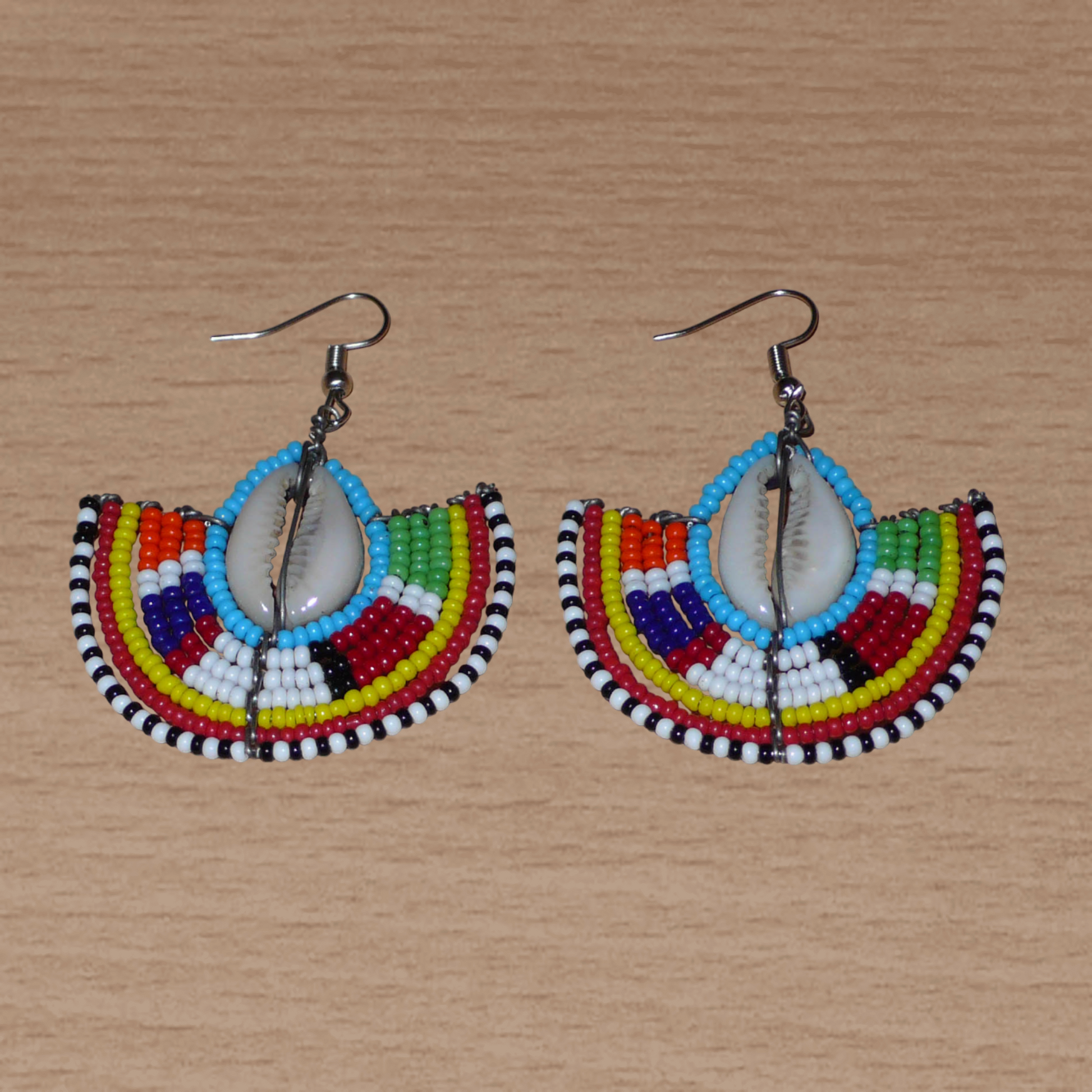 Affirmez votre style et apportez une touche exotique à votre look avec cette paire de boucles d'oreilles africaines Massai issues de l'artisanat traditionnel kenyan. Ces boucles d'oreilles aux accents ethniques chic se composent de perles de rocaille bleues et multicolores et de coquillages cauris. De taille moyenne, elles mesurent 6 cm de long et 4.5 cm de large, et se portent avec des crochets en acier inoxydable sur des oreilles percées.