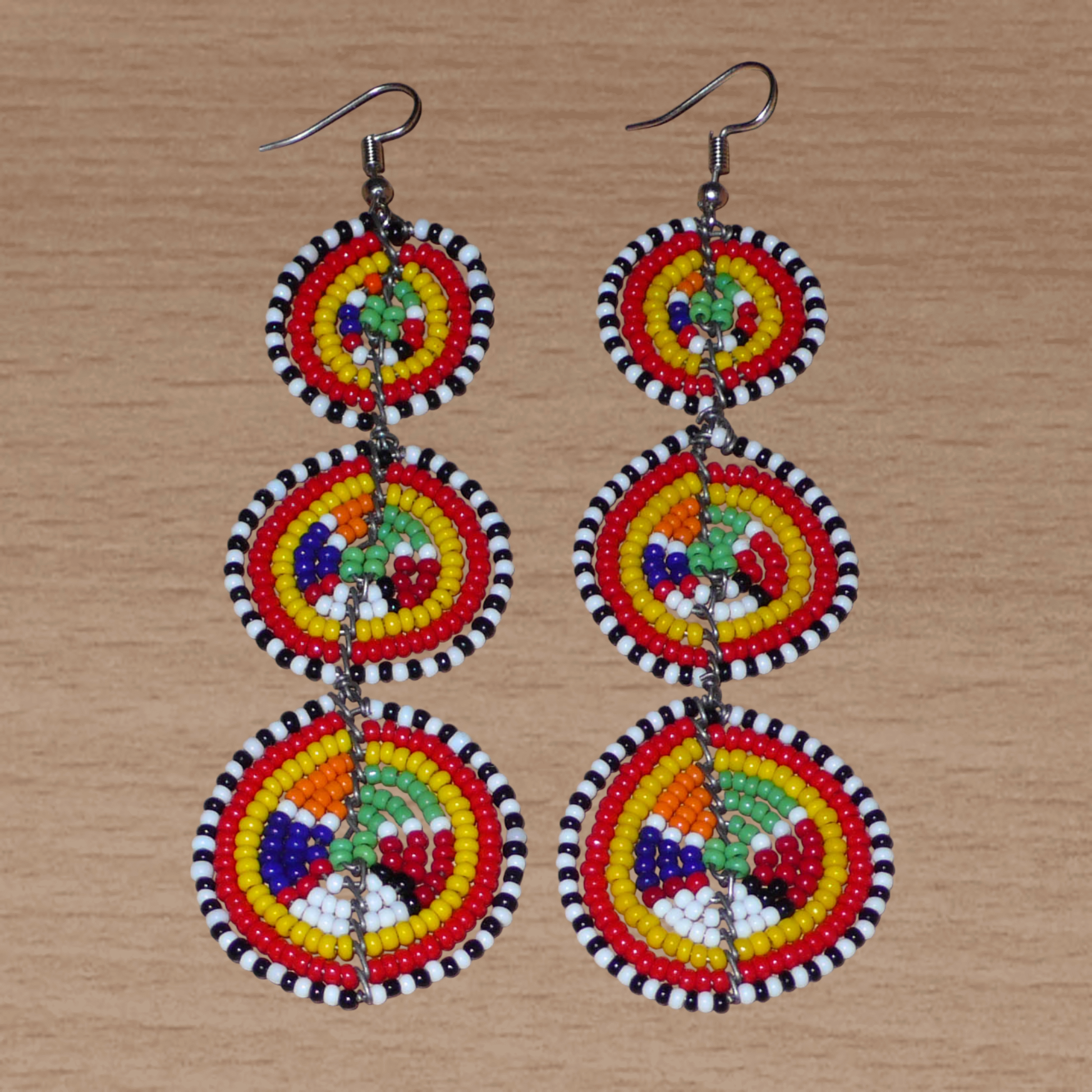Affirmez votre style avec ces boucles d'oreilles africaines traditionnelles de confection artisanale Massai, évoquant le style afro chic des années 70. Elles se composent de perles de rocaille multicolores enfilées sur des fils de fer montés en forme de trois cercles superposés. Ces boucles d'oreilles mesurent 11 cm de long et 3.5 cm de large ; elles se portent avec des crochets en acier inoxydable sur des oreilles percées.