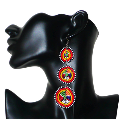 Affirmez votre style avec ces boucles d'oreilles africaines traditionnelles de confection artisanale Massai, évoquant le style afro chic des années 70. Elles se composent de perles de rocaille multicolores enfilées sur des fils de fer montés en forme de trois cercles superposés. Ces boucles d'oreilles mesurent 11 cm de long et 3.5 cm de large ; elles se portent avec des crochets en acier inoxydable sur des oreilles percées.